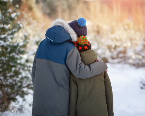A photograph of two children wearing winter clothing hugging in a snowy winter setting