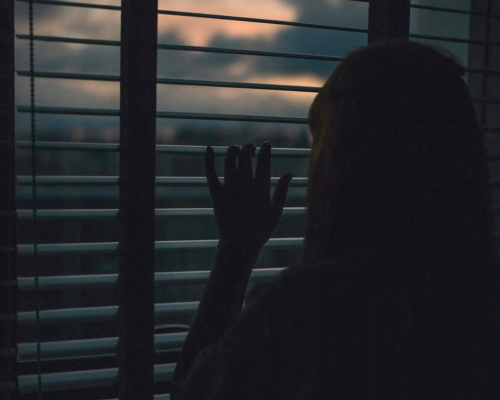 A photo of a girl looking out of a window waiting for someone