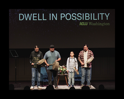 A group of four Indigenous drummers performing on a stage below the words Dwell In Possibility 