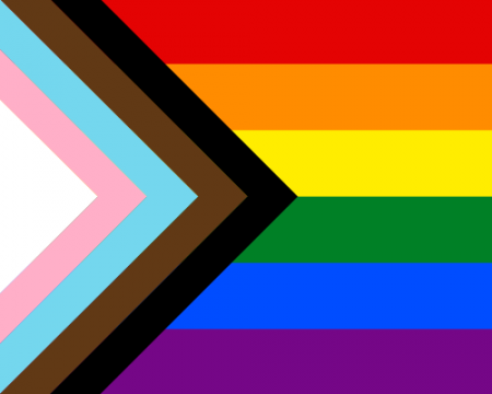 An image of a progress pride flag (Red, orange, yellow, green, blue, and purple rainbow pride flag with an additional a chevron along the hoist that features black, brown, light blue, pink, and white stripes).