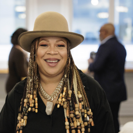 A person with long beaded hair and a tan hat smiling for the camera 