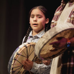 A young person and an adult holding and playing hand drums 