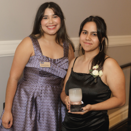 Two people with long dark brown hair smiling for the camera, one holding an award